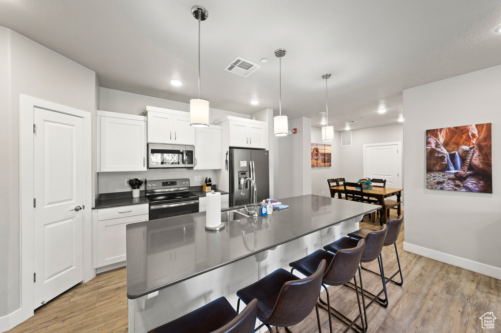 Kitchen featuring stainless steel appliances, light wood-type flooring, dark countertops, a breakfast bar area, and white cabinetry