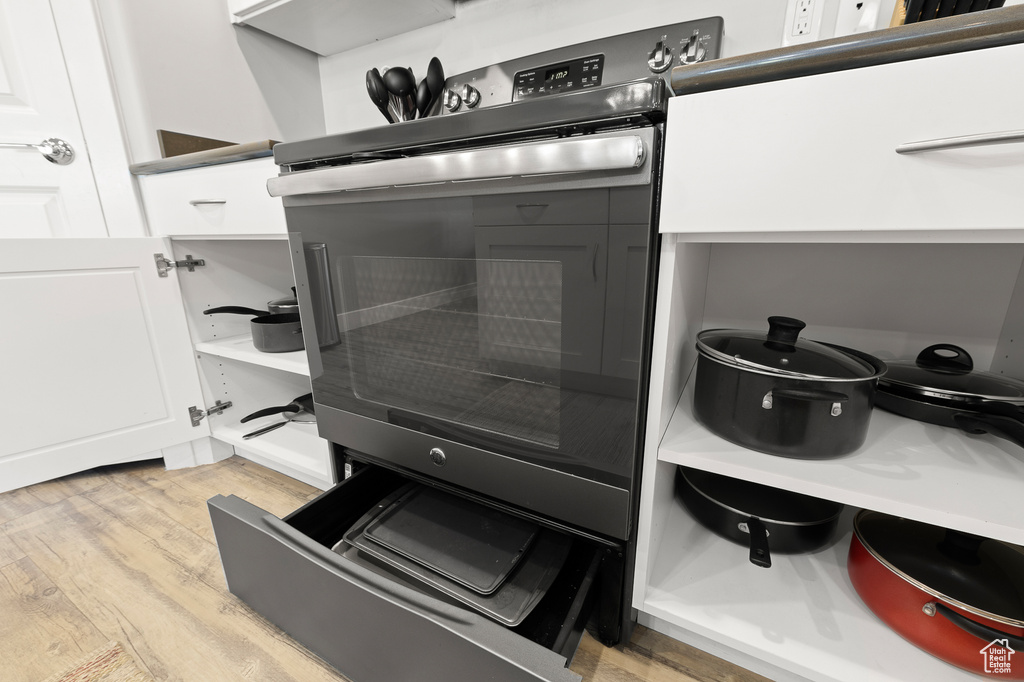 Kitchen view of light wood-style floors, white cabinets, and electric stove