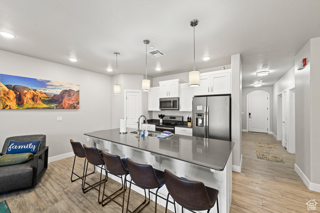 Kitchen with appliances with stainless steel finishes, dark countertops, a breakfast bar area, light wood-type flooring, and recessed lighting