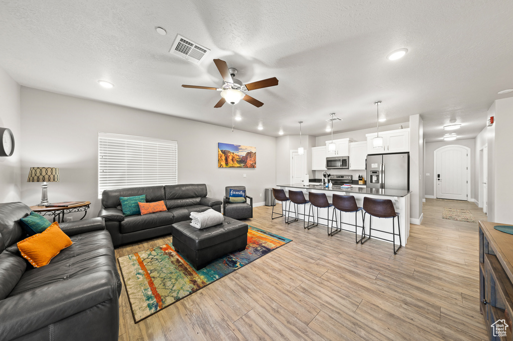 Living room featuring ceiling fan, arched walkways, light wood finished floors, and recessed lighting