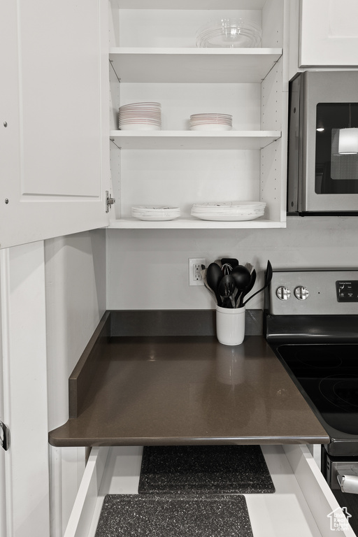 Kitchen view of electric range, open shelves, and white cabinets