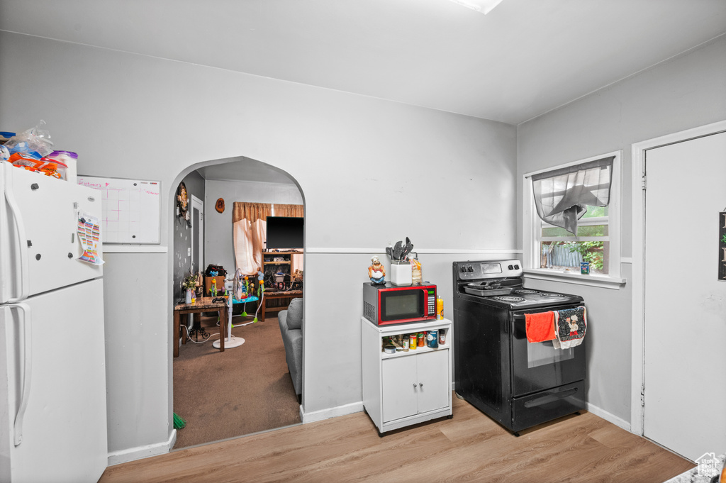 Kitchen with black range with electric cooktop, freestanding refrigerator, light wood-style flooring, and arched walkways