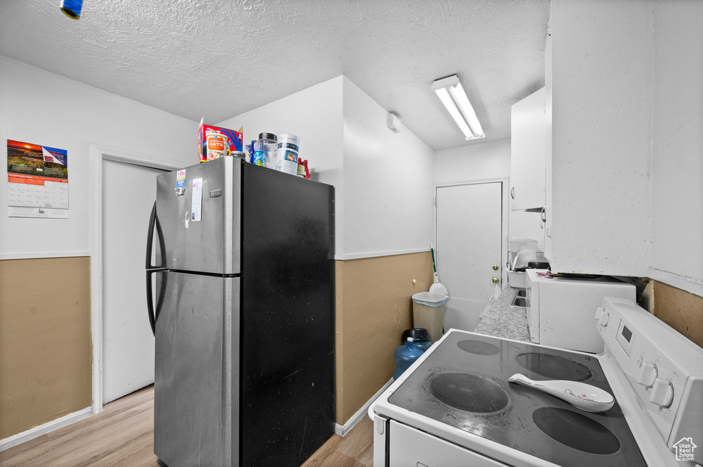 Kitchen with freestanding refrigerator, white electric range oven, light wood finished floors, and a textured ceiling