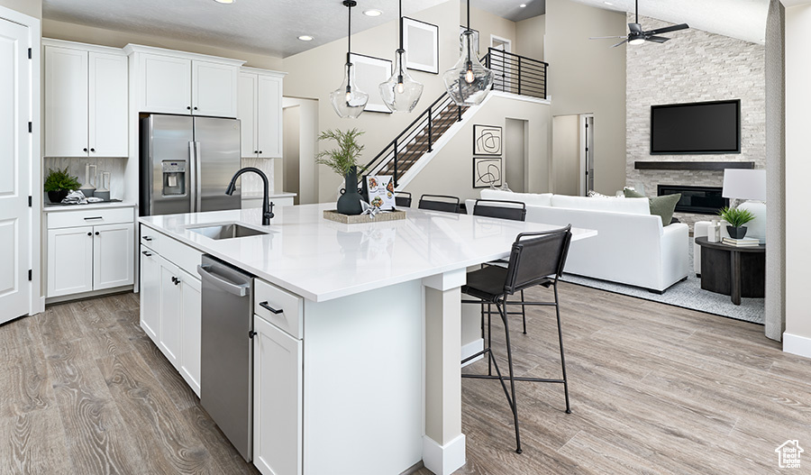 Kitchen with appliances with stainless steel finishes, ceiling fan, light wood-type flooring, white cabinetry, and an island with sink