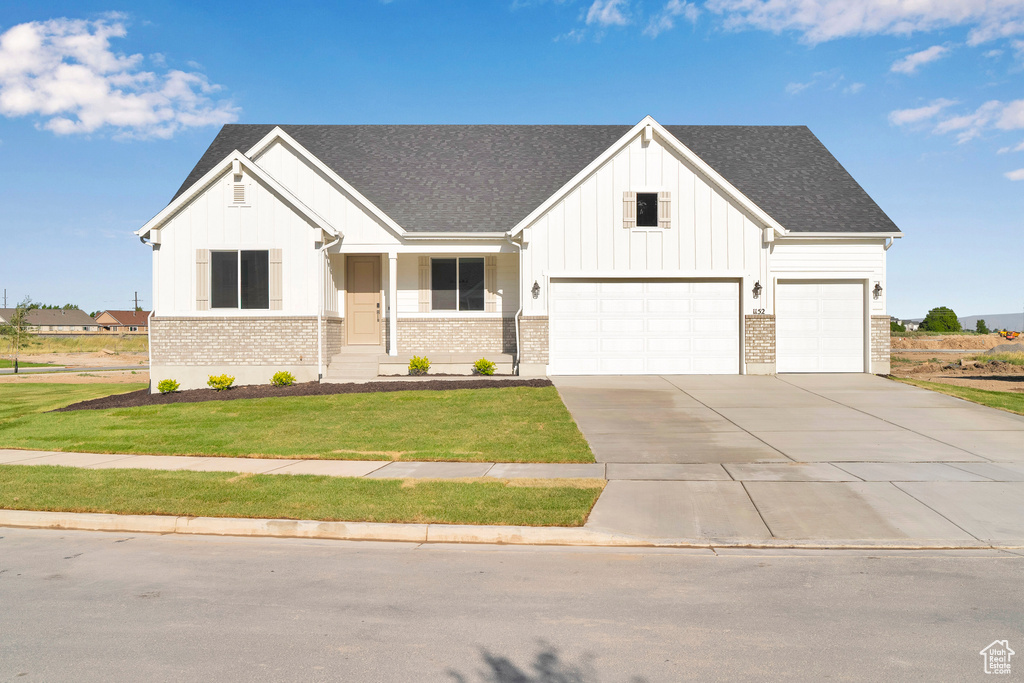 Modern farmhouse with board and batten siding, a front lawn, brick siding, and driveway
