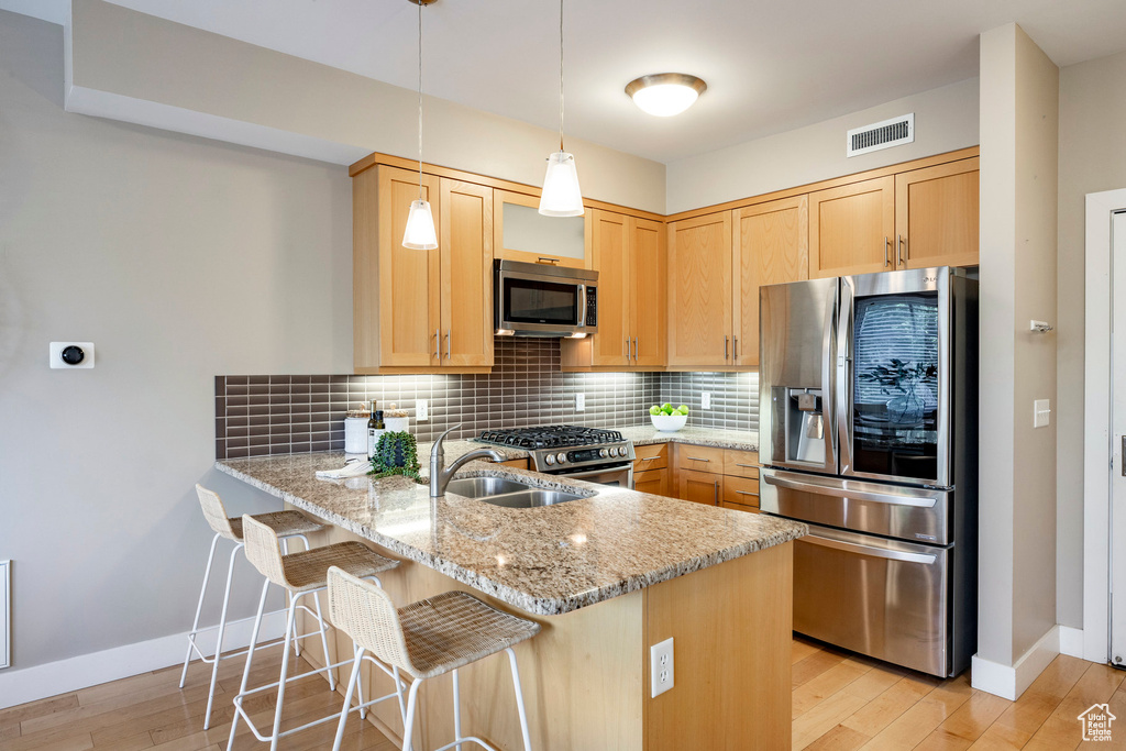 Kitchen featuring appliances with stainless steel finishes, a peninsula, light stone countertops, backsplash, and light wood-type flooring