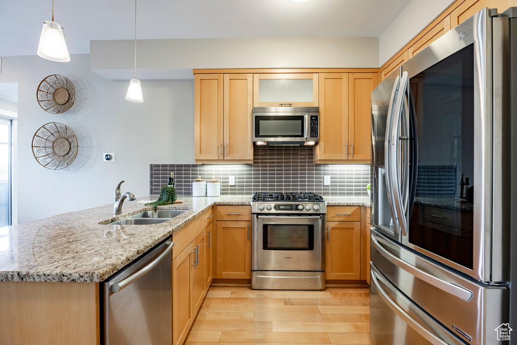 Kitchen with stainless steel appliances, a peninsula, light wood-style flooring, backsplash, and light stone countertops