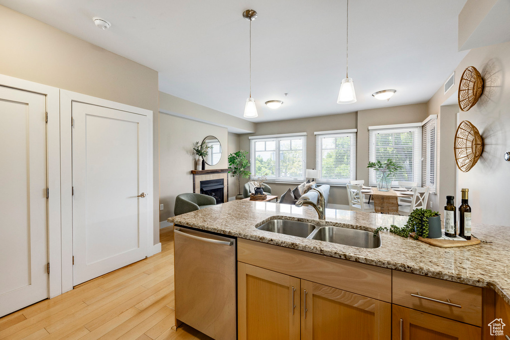 Kitchen featuring stainless steel dishwasher, a tiled fireplace, light wood-style floors, light stone countertops, and hanging light fixtures