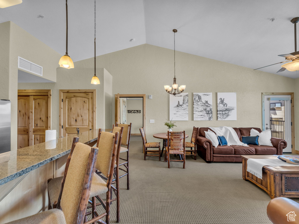 Carpeted living area featuring a chandelier, a ceiling fan, and high vaulted ceiling