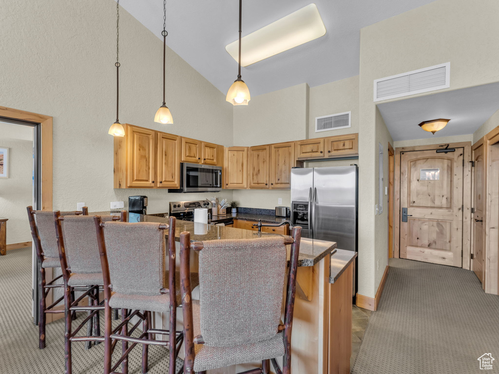 Kitchen featuring stainless steel appliances, high vaulted ceiling, a kitchen bar, light colored carpet, and a peninsula