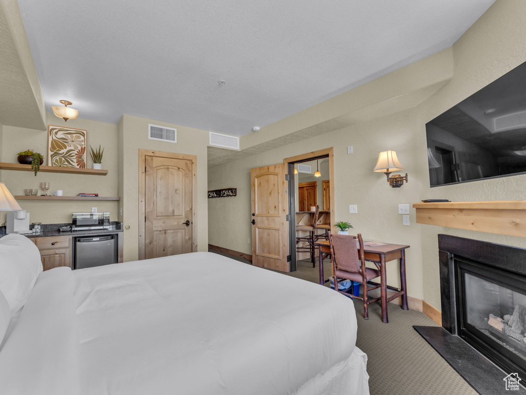 Carpeted bedroom featuring a glass covered fireplace and refrigerator
