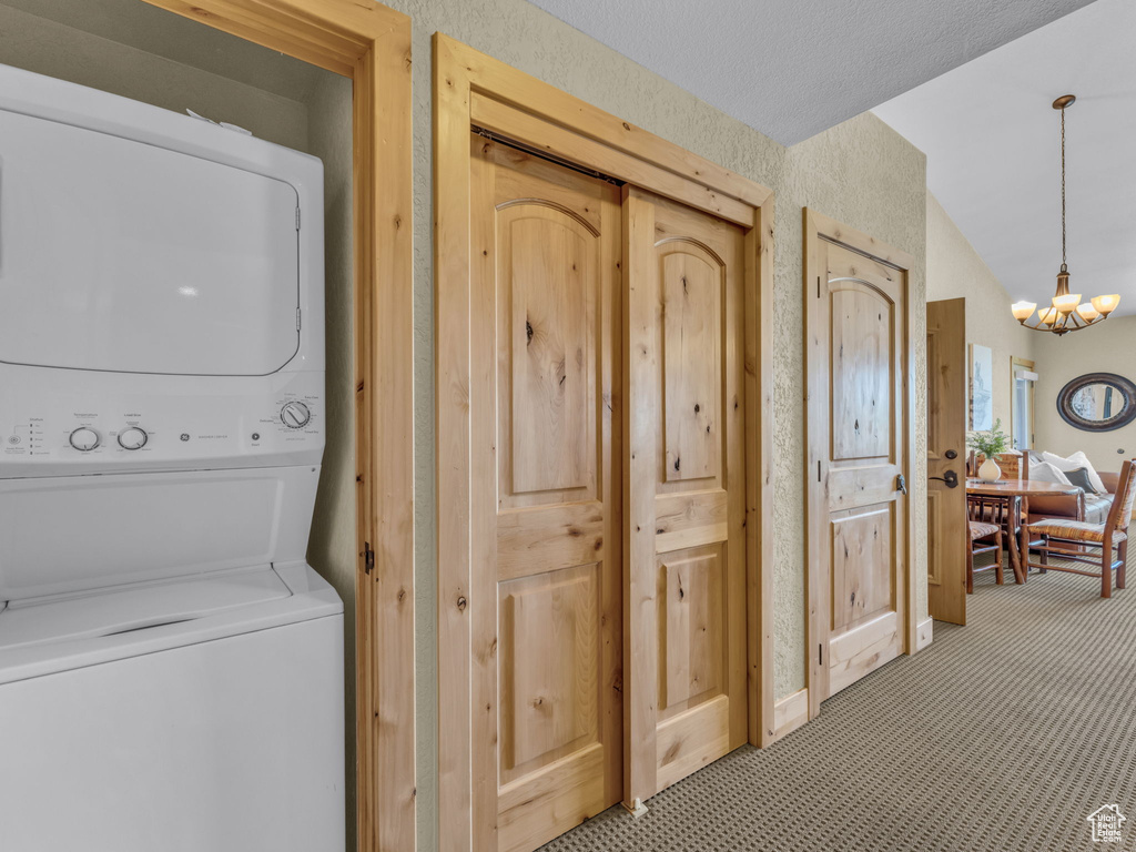 Washroom featuring stacked washer / dryer, a chandelier, and light carpet