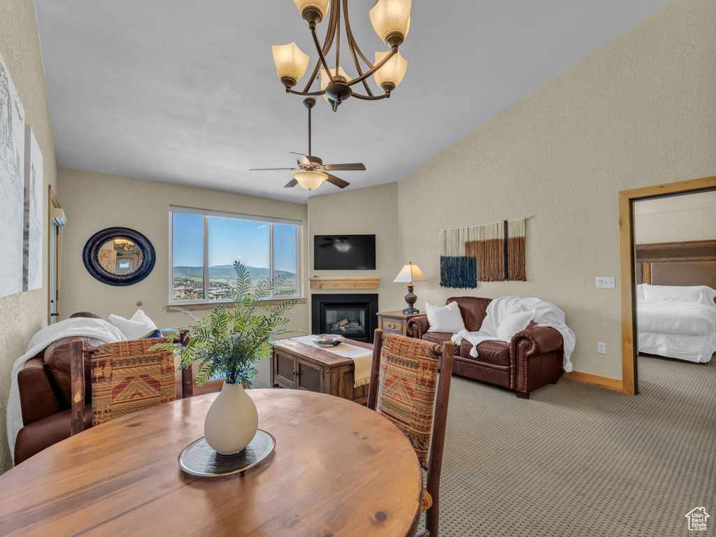 Dining room featuring carpet floors, a chandelier, a glass covered fireplace, a ceiling fan, and a textured wall