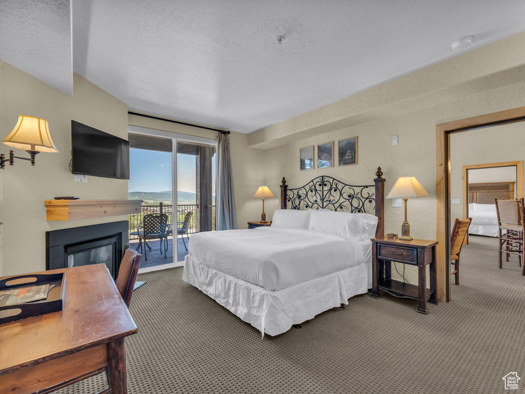 Bedroom with carpet, access to outside, a glass covered fireplace, and a textured ceiling
