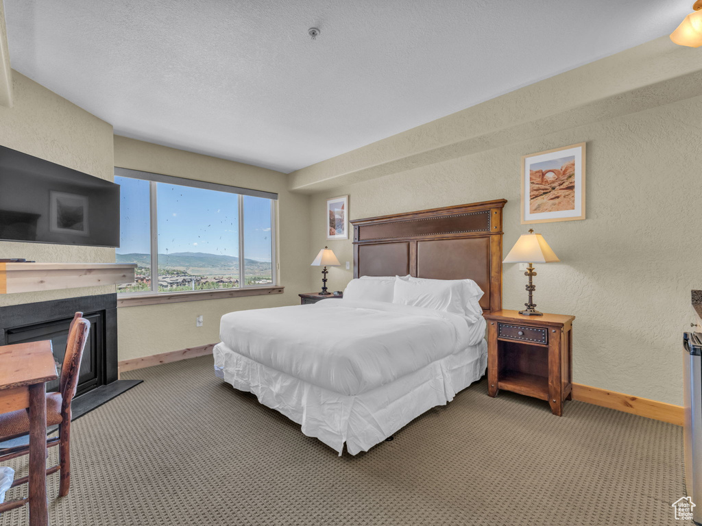 Carpeted bedroom featuring a fireplace with raised hearth and a textured wall