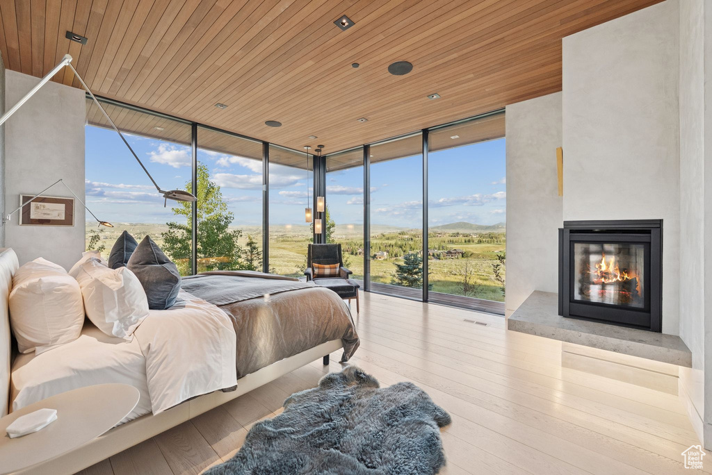 Bedroom with floor to ceiling windows, wooden ceiling, access to exterior, hardwood / wood-style flooring, and a glass covered fireplace