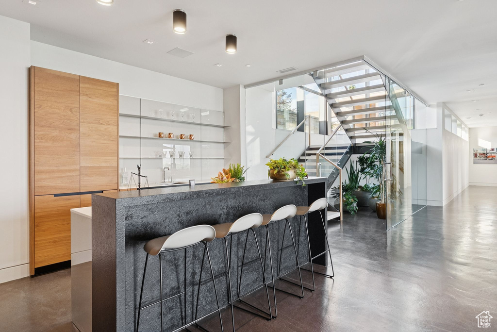 Indoor bar with a wall of windows, stairs, finished concrete flooring, and recessed lighting