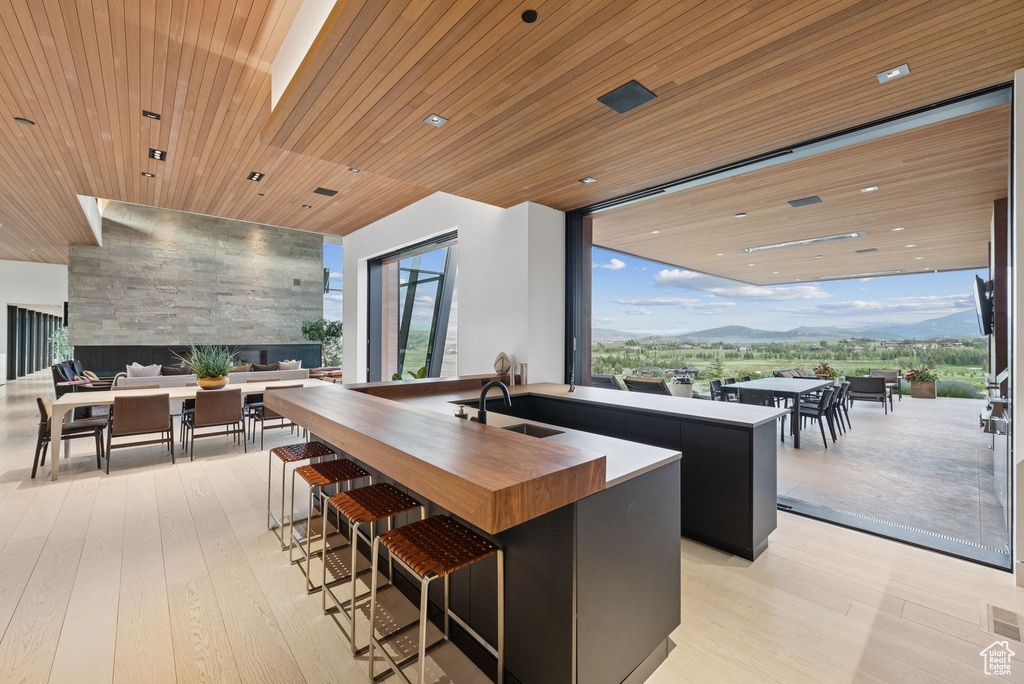 Kitchen featuring butcher block countertops, a kitchen island with sink, light wood finished floors, wood ceiling, and plenty of natural light