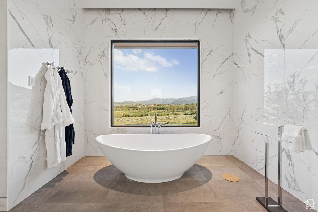 Full bathroom featuring stone wall, a soaking tub, and a mountain view