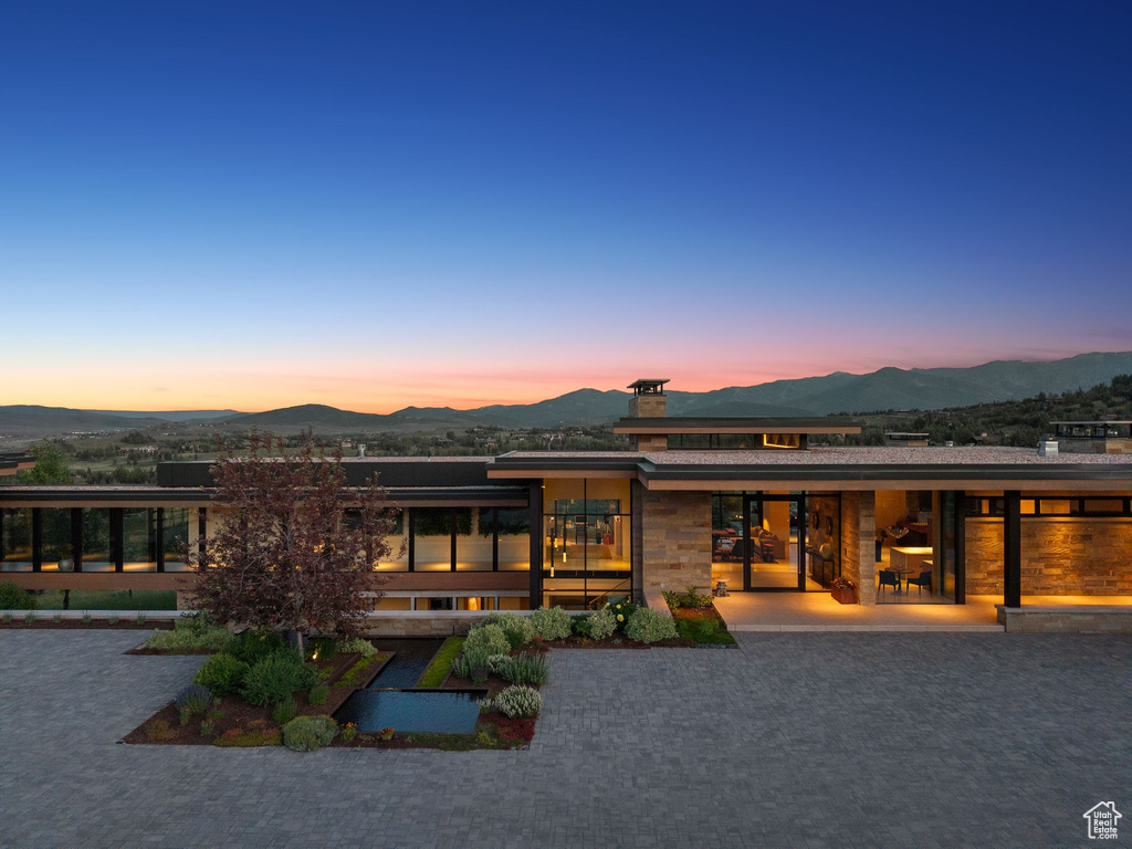 Back of house at dusk with a mountain view, a chimney, and stone siding