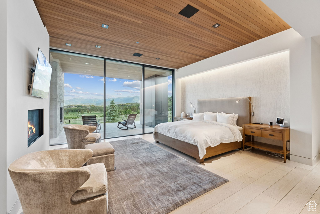 Bedroom with access to exterior, wood ceiling, a wall of windows, wood finished floors, and a lit fireplace