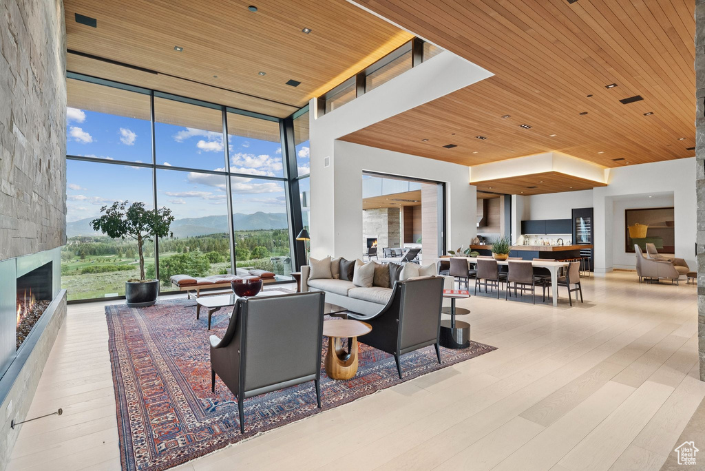 Living room with a mountain view, wooden ceiling, floor to ceiling windows, wood finished floors, and a stone fireplace