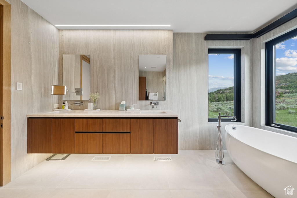 Full bath with double vanity, plenty of natural light, a soaking tub, and tile patterned floors