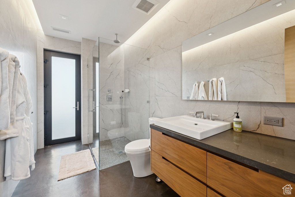 Full bath with tile walls, a marble finish shower, vanity, and finished concrete floors