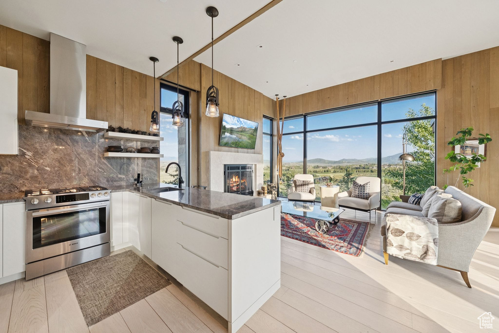 Kitchen with stainless steel gas range oven, wall chimney exhaust hood, wooden walls, modern cabinets, and dark stone counters