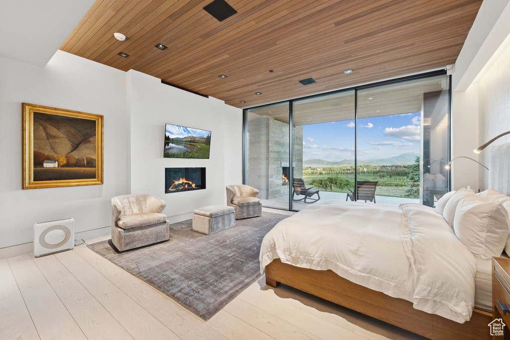 Bedroom with access to outside, wooden ceiling, wood finished floors, floor to ceiling windows, and a warm lit fireplace