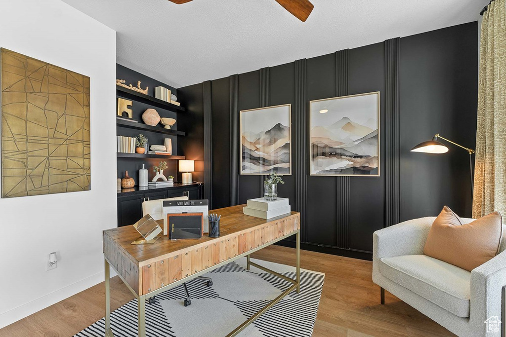 Office space with light wood-type flooring, a ceiling fan, and a decorative wall