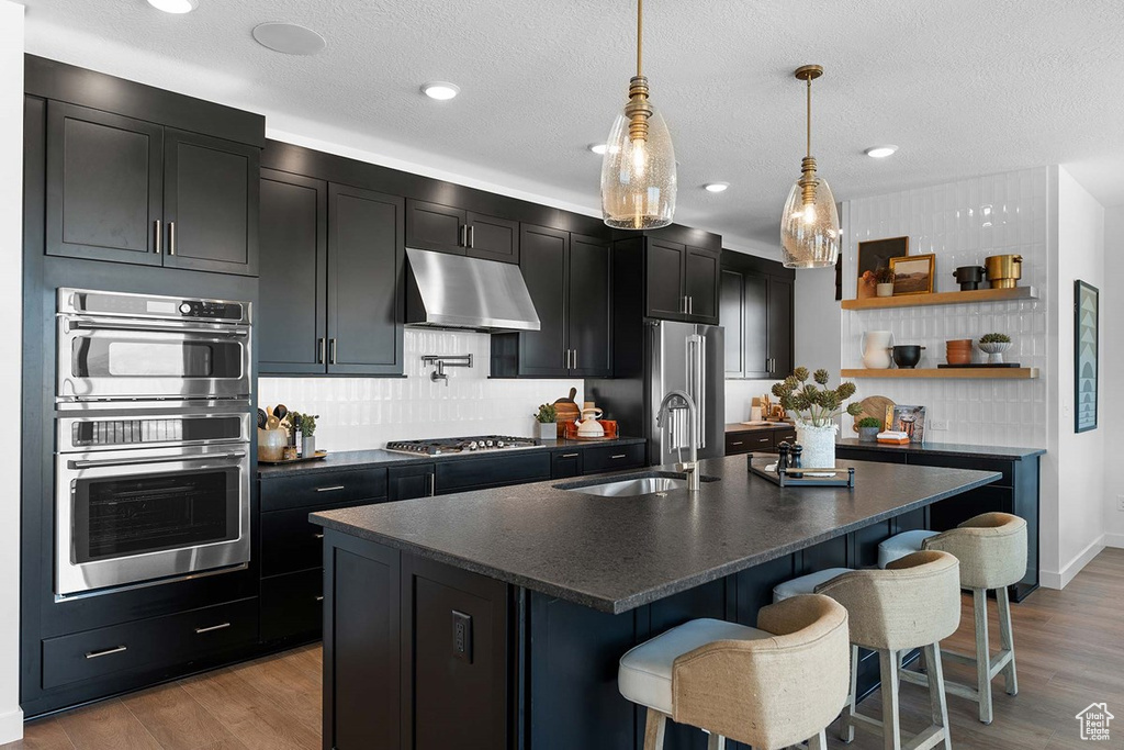 Kitchen with under cabinet range hood, dark countertops, dark cabinetry, stainless steel appliances, and a textured ceiling