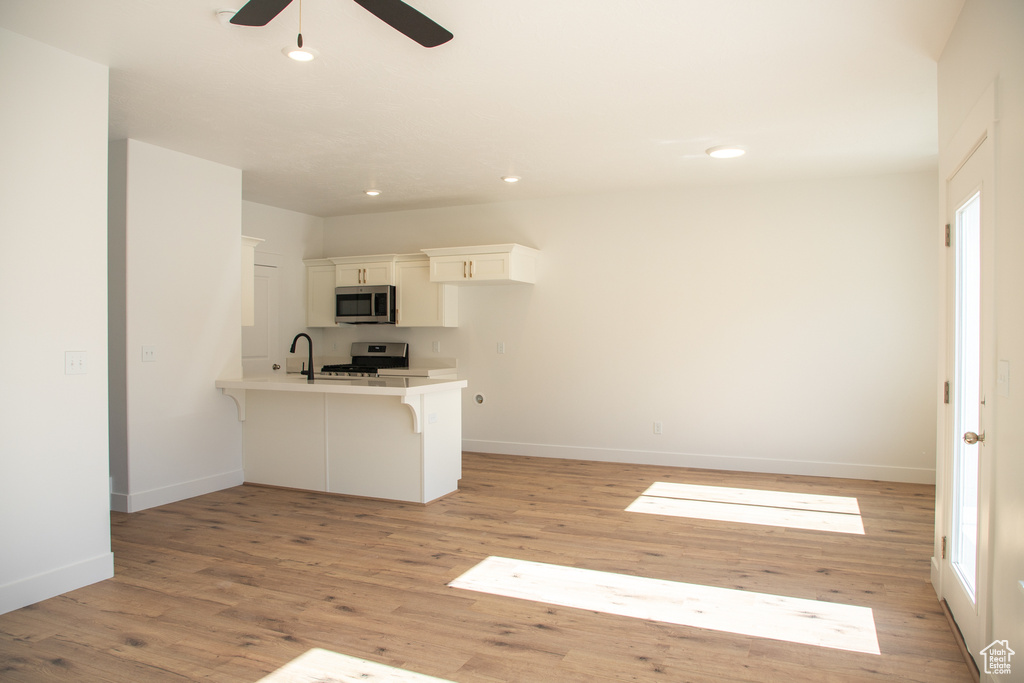 Kitchen featuring a peninsula, a kitchen bar, ceiling fan, light wood-type flooring, and light countertops
