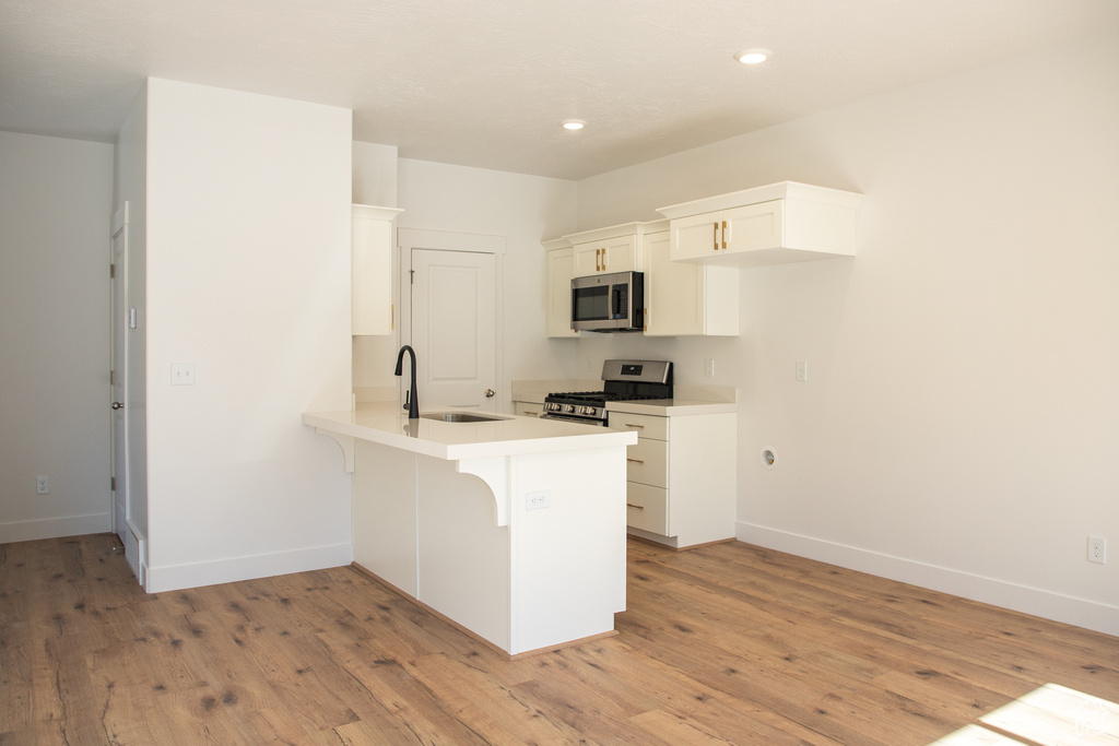 Kitchen featuring a peninsula, appliances with stainless steel finishes, white cabinets, a breakfast bar area, and light wood finished floors