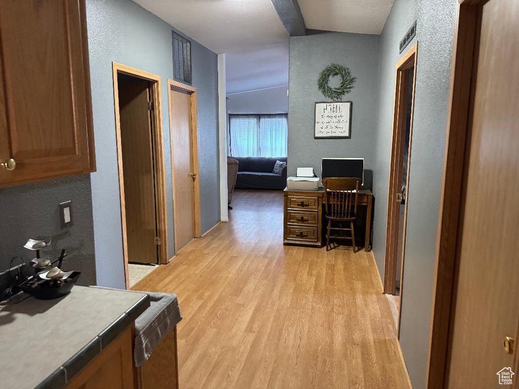 Hallway featuring a textured wall, light wood-style floors, and an office area