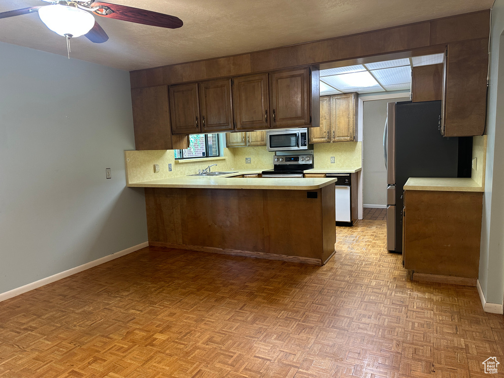 Kitchen with stainless steel appliances, light countertops, a peninsula, a ceiling fan, and decorative backsplash