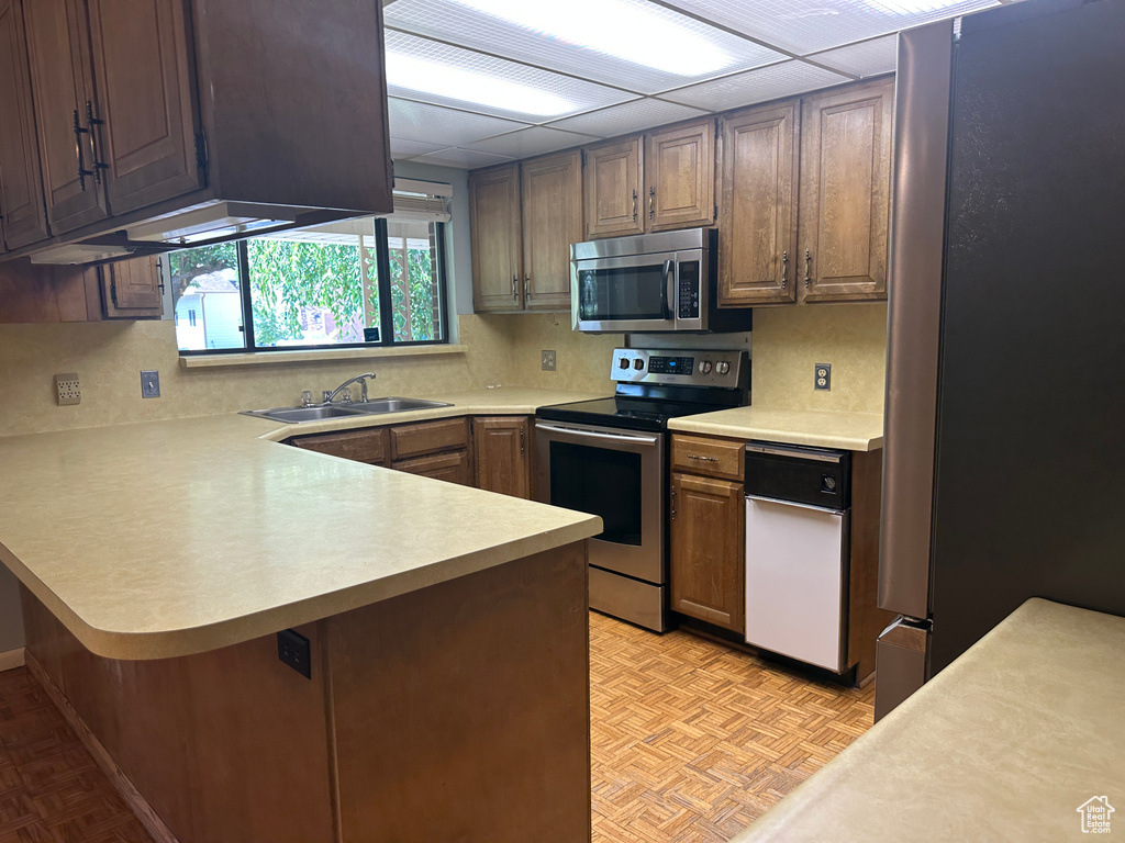 Kitchen with appliances with stainless steel finishes, light countertops, a peninsula, and decorative backsplash