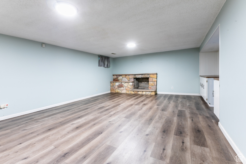 Unfurnished living room featuring a stone fireplace, wood finished floors, and a textured ceiling