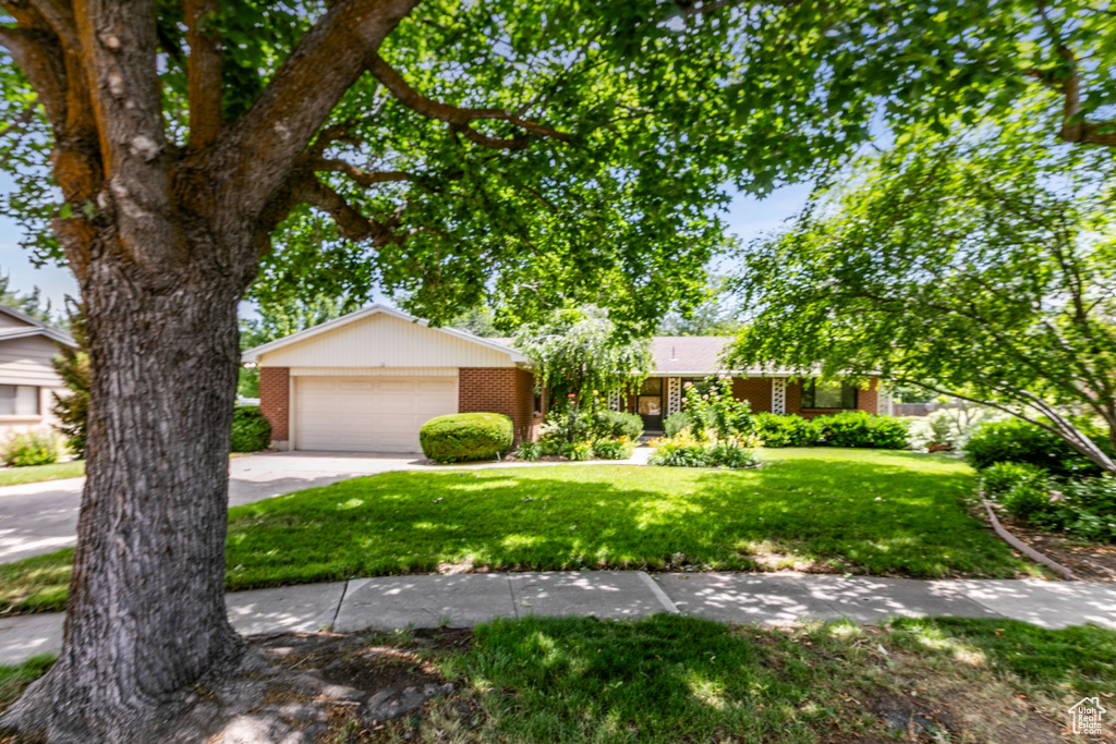 View of front of home featuring brick siding, a front yard, a garage, and driveway