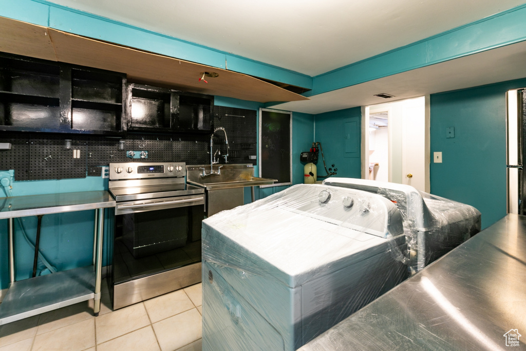 Kitchen featuring stainless steel electric range oven, stainless steel countertops, tile patterned flooring, and washer / dryer