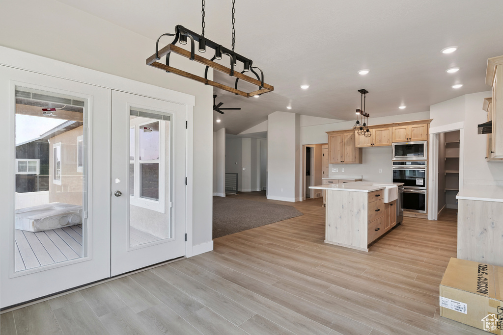 Kitchen with stainless steel appliances, light brown cabinetry, light countertops, french doors, and a kitchen island