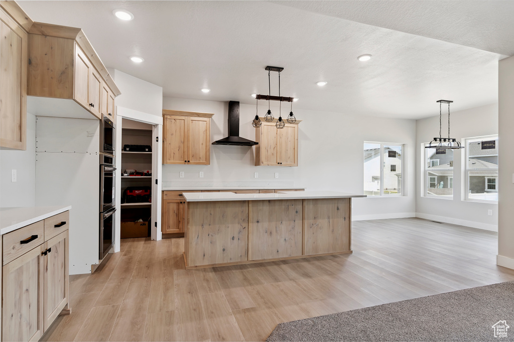 Kitchen with wall chimney exhaust hood, light brown cabinets, light wood-style floors, light countertops, and recessed lighting