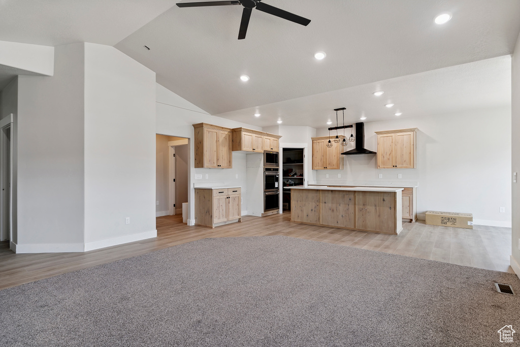 Kitchen with wall chimney range hood, light brown cabinetry, light wood-type flooring, appliances with stainless steel finishes, and ceiling fan