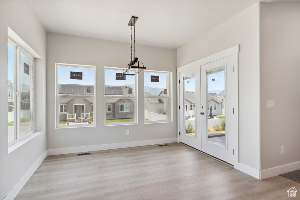 Unfurnished dining area featuring plenty of natural light, french doors, a chandelier, and light wood-style floors