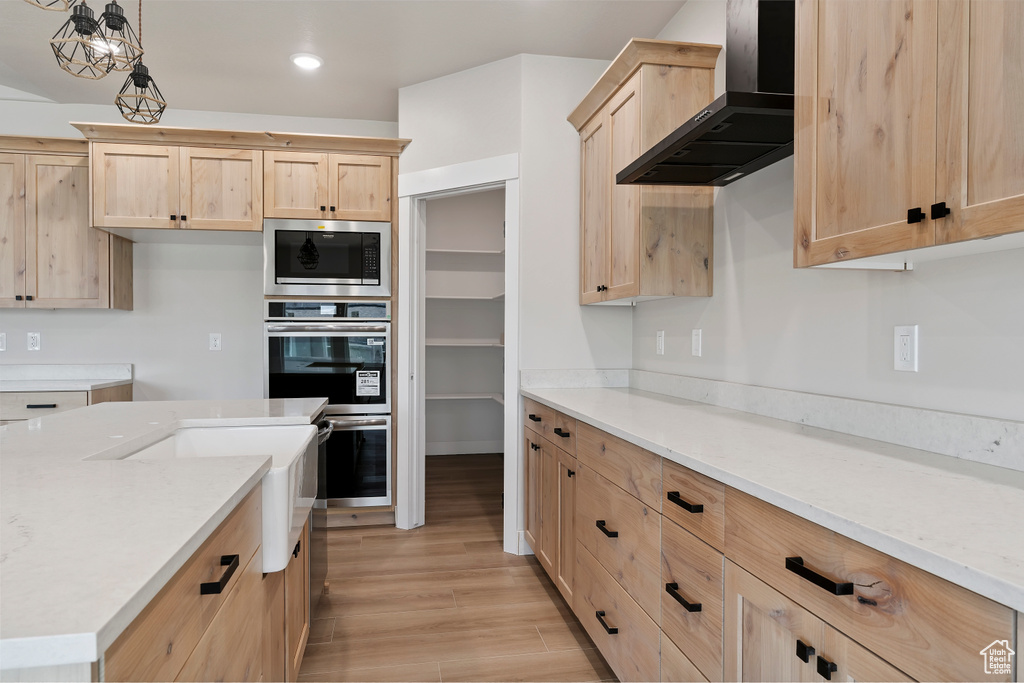 Kitchen with wall chimney exhaust hood, light brown cabinetry, stainless steel appliances, recessed lighting, and light wood finished floors