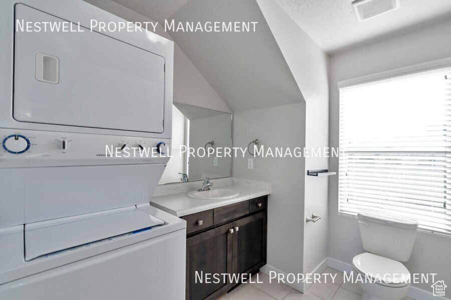 Bathroom with stacked washer / drying machine, vanity, plenty of natural light, tile patterned floors, and vaulted ceiling