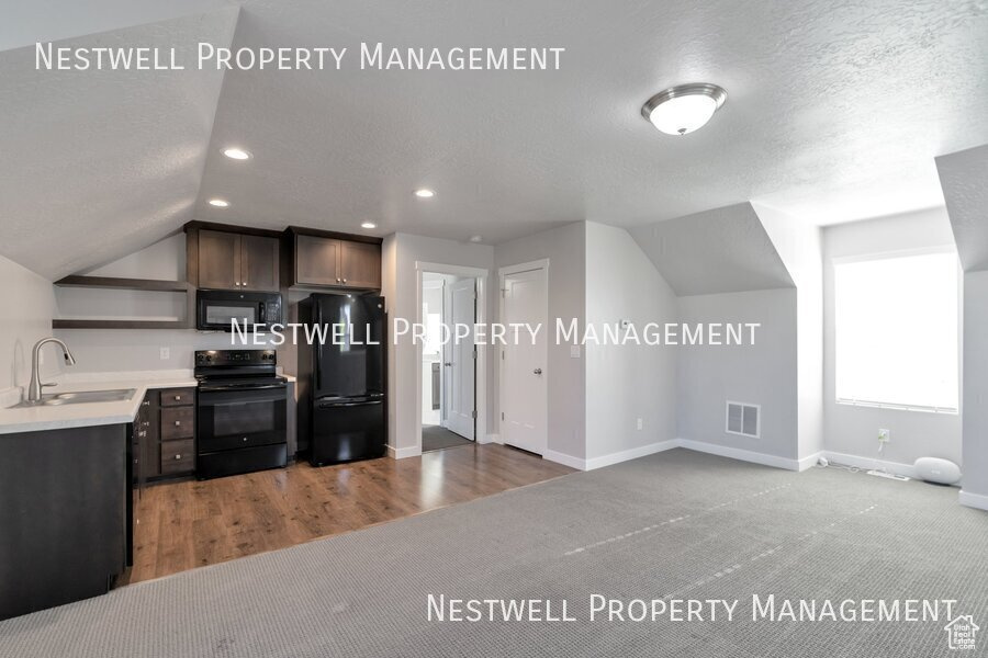 Kitchen featuring black appliances, open shelves, vaulted ceiling, light countertops, and carpet flooring