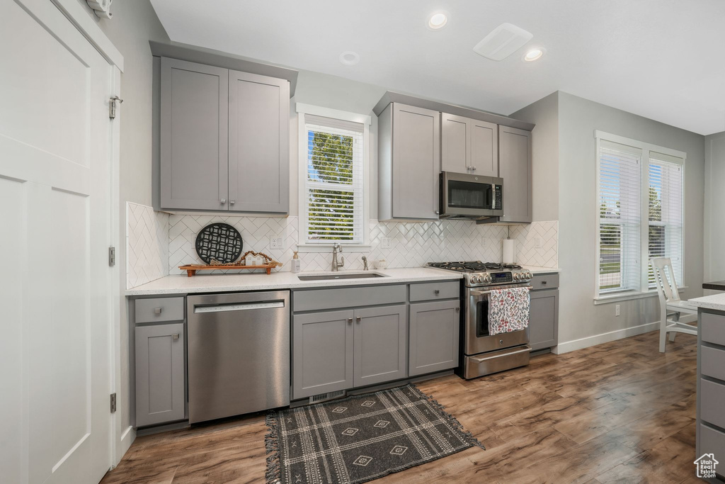Kitchen featuring stainless steel appliances, gray cabinetry, wood finished floors, tasteful backsplash, and recessed lighting