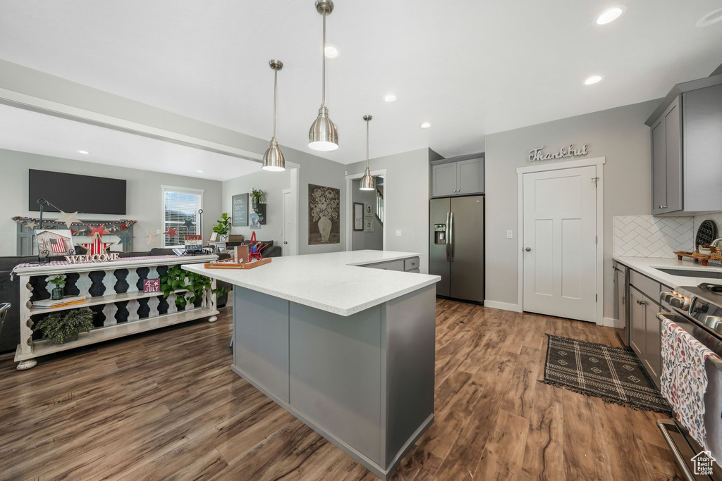 Kitchen featuring stainless steel appliances, gray cabinets, dark wood-style flooring, light countertops, and a kitchen island
