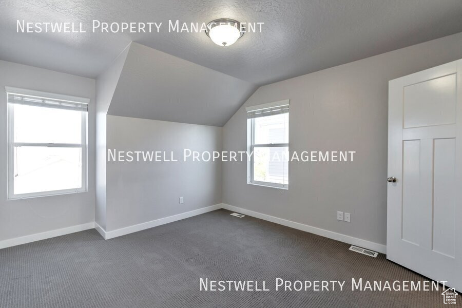 Bonus room with dark colored carpet, vaulted ceiling, and a textured ceiling